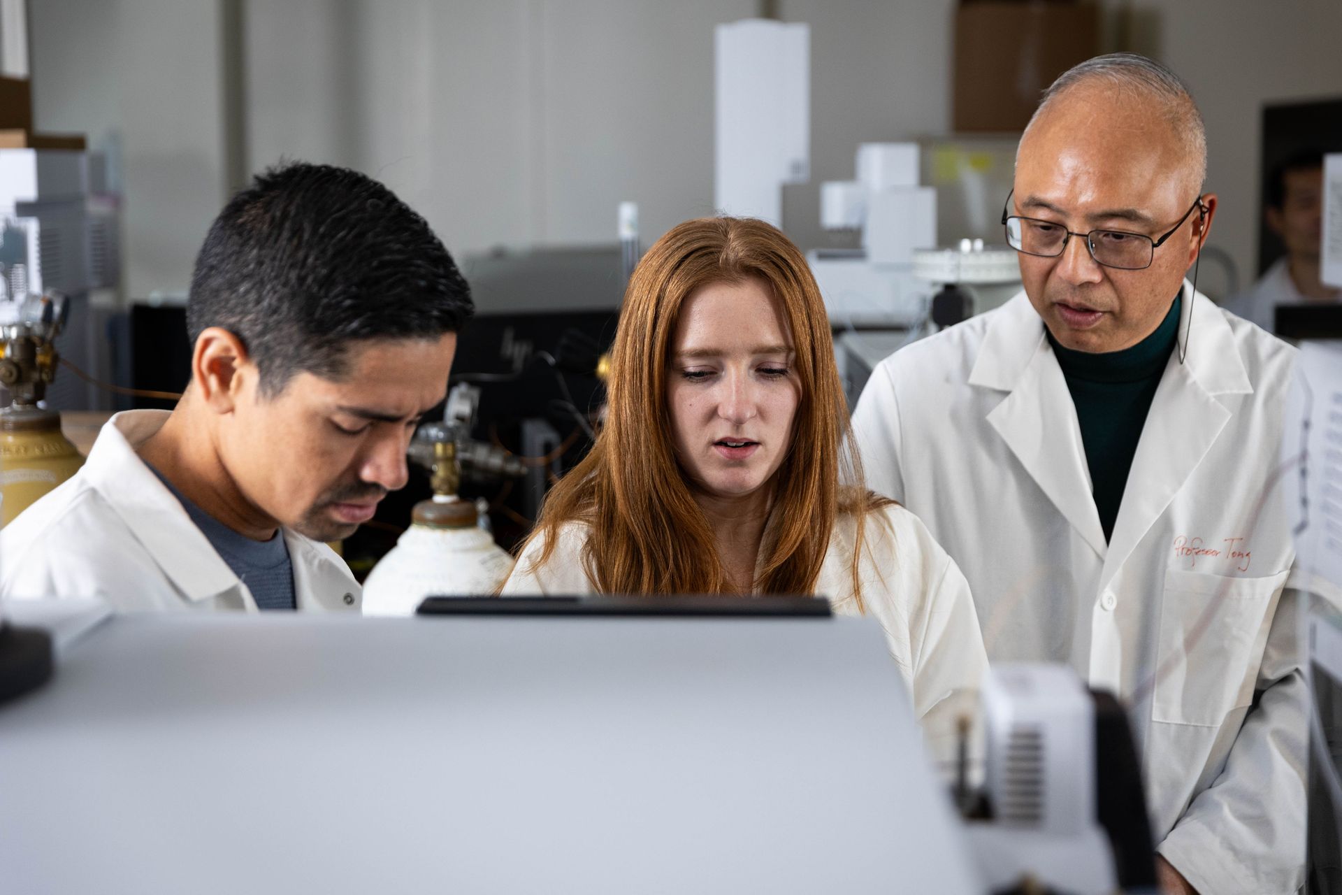 A professor and two students look at a piece of lab equipment together.